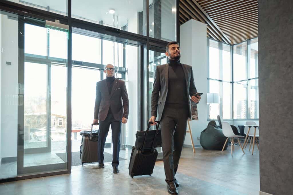 Two elegant business travelers pulling suitcases while entering hotel lounge